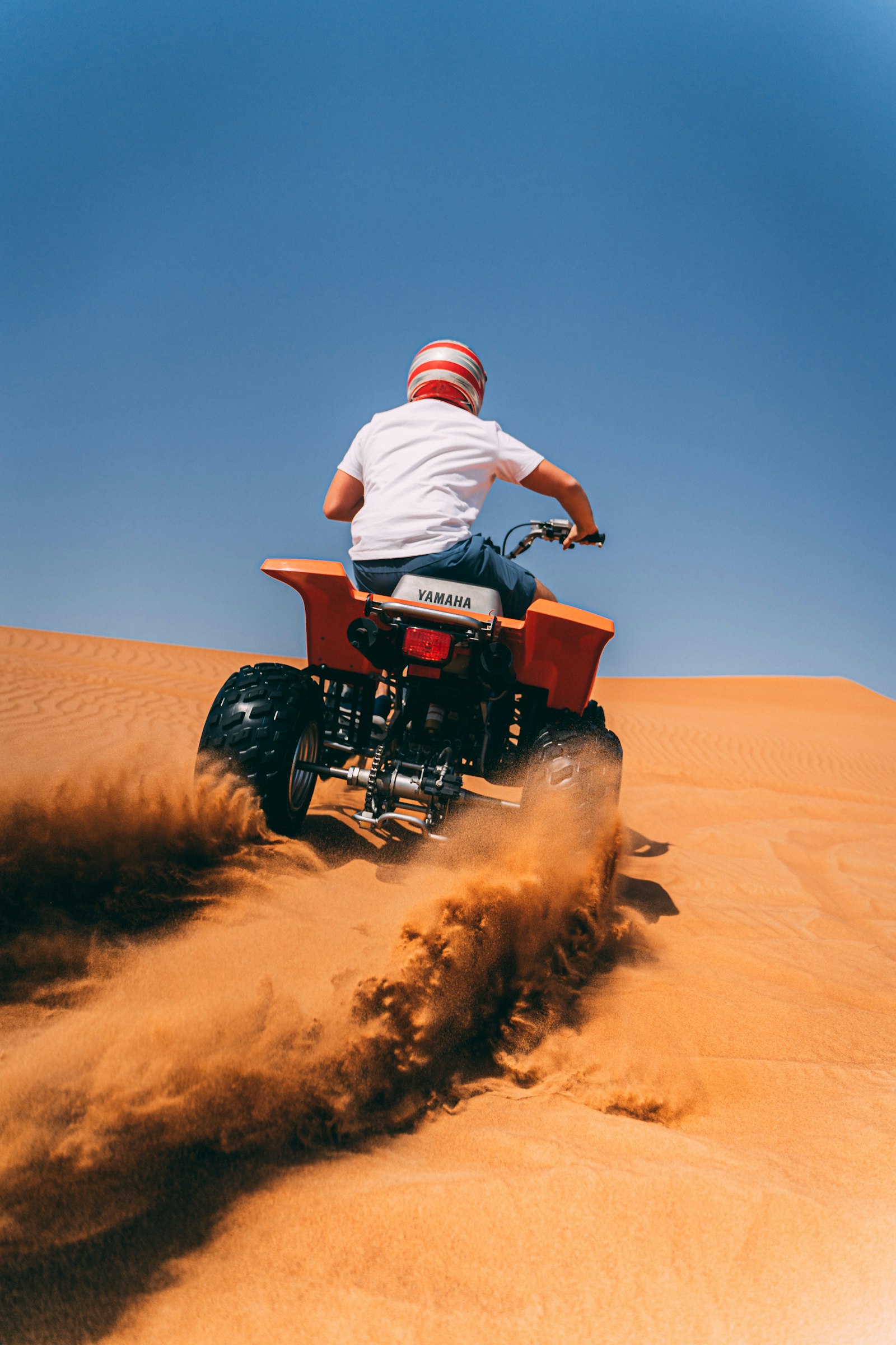A rider on an ATV kicking up dust on a sunny desert trail